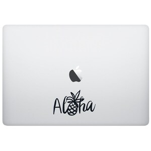 May include: A silver laptop with a black and white Apple logo and a black sticker that says "Aloha" with a pineapple design.
