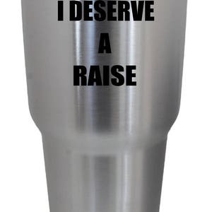 Peut inclure: Un gobelet en acier inoxydable avec une inscription noire qui dit "I DESERVE A RAISE".