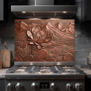 May include: Copper-colored kitchen backsplash featuring a detailed relief of a desert landscape. A large lotus flower is central, with cacti and mountains in the background. The backsplash is mounted above a stainless steel gas range.