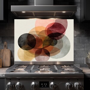 May include: A decorative kitchen backsplash featuring an abstract design of overlapping circles in shades of black, brown, orange, and red. The artwork is mounted above a stainless steel gas range.