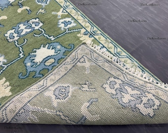 Könnte beinhalten: Ein grün-blau gemusterter Teppich mit floralem Design. Der Teppich ist teilweise aufgerollt und zeigt die Unterseite mit einem ähnlichen Muster in einer helleren Farbe. Der Teppich hat einen Fransenrand.
