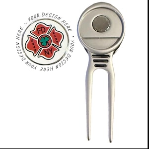 Op de afbeelding: Een zilveren golfdivot-reparatietool met een magnetische balmarker. De marker heeft een rood-wit ontwerp met de tekst "FD NY" en "YOUR DESIGN HERE" rondom. De tool heeft een vork met twee tanden.