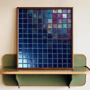 May include: A square wall art piece with a wooden frame. The artwork features a grid of small, iridescent blue tiles that shift in color. The tiles are arranged in a gradient, transitioning from dark blue to lighter shades with hints of purple and silver.