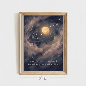 May include: A framed wall art print featuring a celestial scene with a central glowing sun surrounded by orbital rings and small planets against a dark, cloudy nebula background. The text reads: your orbit is shaped by what you pull close.