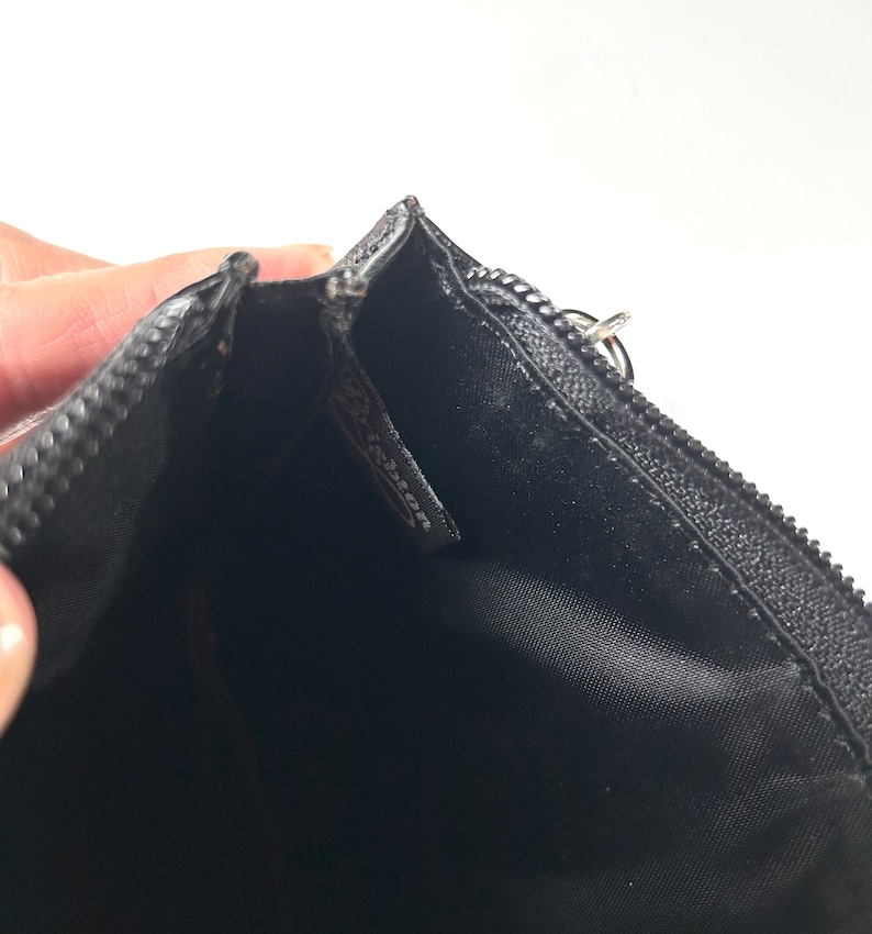 以下が含まれることがあります： シルバーのジッパープルが付いた黒いジッパーポーチ。内側は黒い生地です。「Brighton」のブランド名がポーチ内の小さなタグに表示されています。