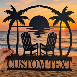 May include: A black metal wall art piece featuring a circular frame with a silhouette of two Adirondack chairs, two palm trees, and a sun setting over the ocean. The bottom section includes the cut-out text CUSTOM TEXT in a bold font.