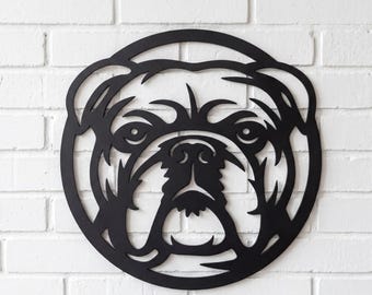 May include: A circular black metal wall art piece featuring a stylized cutout design of a bulldog face. The artwork displays the distinct facial features of the dog, including its ears, eyes, and snout, all rendered in a solid matte black finish.