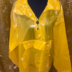 K&ouml;nnte beinhalten: Ein leuchtend gelber, transparenter Regenmantel mit Kragen und Knopfverschl&uuml;ssen. Der Regenmantel hat zwei Vordertaschen und eine Schl&uuml;sselanh&auml;nger-Halskette. Das Kleidungsst&uuml;ck wird auf einer schwarzen Schaufensterpuppe pr&auml;sentiert.
