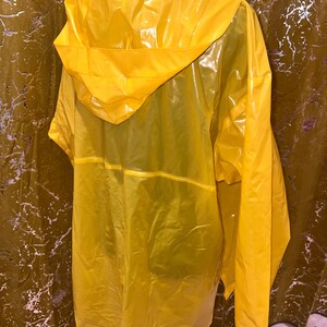 K&ouml;nnte beinhalten: Ein leuchtend gelber Regenmantel mit Kapuze. Der Regenmantel besteht aus einem gl&auml;nzenden, wasserdichten Material. Die Kapuze ist gro&szlig; und bedeckt die Schultern. Der Mantel ist so konzipiert, dass er &uuml;ber der Kleidung getragen wird, um vor Regen zu sch&uuml;tzen.