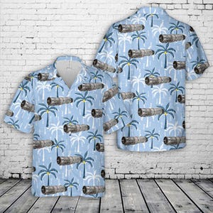 May include: Light blue short-sleeve button-down shirt with a pattern of palm trees and jet engines. The shirt is displayed with a matching shirt, both on a white brick wall background.