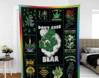 May include: Black blanket with a rainbow border featuring cannabis-themed graphics and text. The design includes a green bear smoking, marijuana leaves, and phrases like "Born Stoned" and "Don't Care."