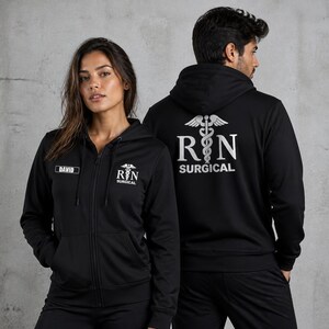 Puede incluir: Una sudadera negra con cremallera, capucha y cordón, que presenta un símbolo de caduceo blanco y el texto RN SURGICAL en el pecho y la espalda. La parte delantera incluye una etiqueta rectangular con el nombre DAVID impreso en letras blancas.