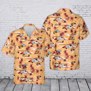 May include: A short-sleeved button-down shirt in a light orange hue featuring an all-over print of white and red helicopters interspersed with dark pink palm trees and small island motifs. The shirt has a classic collar and a front button placket.