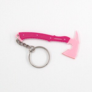May include: A pink and fuchsia axe-shaped keyring. The axe head is a lighter shade of pink, while the handle is fuchsia with small, circular details. A silver chain and keyring are attached.