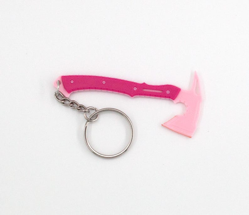 May include: A pink and fuchsia axe-shaped keyring. The axe head is a lighter shade of pink, while the handle is fuchsia with small, circular details. A silver chain and keyring are attached.