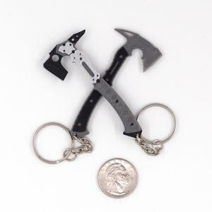 Puede incluir: Dos llaveros de hacha en miniatura con llaveros plateados. Un hacha es negra y plateada, la otra es gris y negra. Se incluye una moneda para comparar el tamaño. Las hachas tienen mangos texturizados.