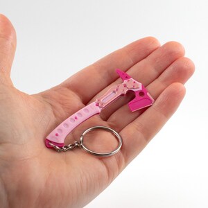May include: A miniature pink and light pink axe keychain. The axe head is a bright pink, and the handle is light pink with small holes. A silver key ring is attached. The axe is a novelty item.