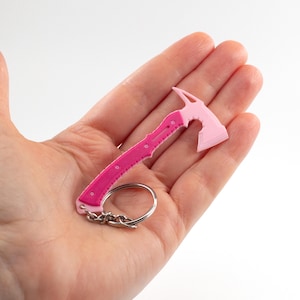 May include: A pink and magenta miniature axe keyring. The axe head is light pink, and the handle is magenta with circular details. A silver keyring and chain are attached.