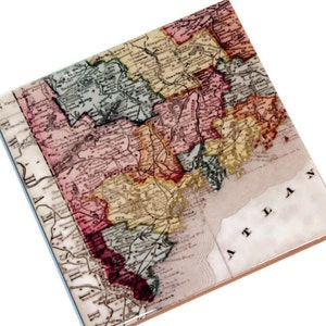 May include: An antique map of New England, printed on a ceramic coaster. The map shows the states of New Hampshire, Vermont, Massachusetts, Rhode Island, and Connecticut. The map is in shades of pink, yellow, green, and blue.