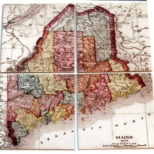 May include: Four vintage-style ceramic coasters featuring a detailed map of Maine, divided into four sections. The map is in shades of brown, red, yellow, and green, with the text "MAINE SCALE" and "Statute Miles 20 = 1 Inch" visible at the bottom.