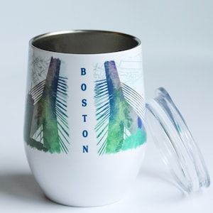 May include: White stainless steel travel mug with a green, blue, and purple watercolor design of the Zakim Bunker Hill Bridge in Boston, Massachusetts. The word "BOSTON" is printed vertically on the mug in blue.
