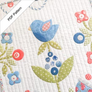 May include: A quilted fabric panel featuring a central blue bird applique surrounded by floral motifs in shades of coral, green, and blue. The design includes various patterned fabric shapes, circular accents, and straight-line quilting. Text reads PDF Pattern.