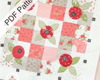 May include: A square quilt featuring a grid of patchwork squares in shades of red, pink, white, and grey with floral and gingham patterns. Appliqué red circular flowers with green leaves are centered on specific blocks. Text reads PDF Pattern.