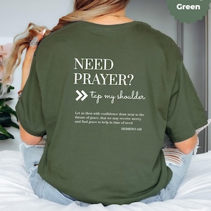 Könnte beinhalten: Militärgrünes T-Shirt mit dem weißen Text "NEED PRAYER? tap my shoulder". Auf der Rückseite des Shirts befindet sich auch ein Bibelvers. Das Shirt hat eine lockere Passform und ist aus weichem Material gefertigt.