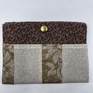 May include: A fabric wallet with a floral pattern on the inside flap and a gold snap closure. The exterior features a patchwork design with beige and olive green floral and geometric patterns.