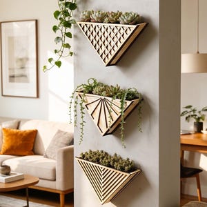 Peut inclure: Trois jardinières murales triangulaires en bois avec des motifs géométriques, chacune remplie de plantes succulentes et de plantes retombantes. Les jardinières sont montées sur un mur gris clair, créant une esthétique moderne et minimaliste.