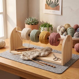 May include: A wooden yarn holder with four colorful yarn skeins in cream, green, yellow, and pink. Knitting needles, crochet hooks, and a pair of scissors sit on a gray felt mat. A partially knitted sock is also visible.