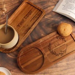 May include: Two wooden serving trays with a coffee cup and a biscuit. One tray has the text "Your Logo" engraved, the other has "Dad's Coffee & Biscuits" with a leaf design. The items are on a wooden surface.