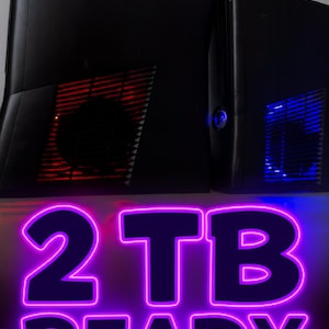 May include: Two black computer towers with illuminated vents. One has red lighting, the other blue. The text "2 TB READY" is displayed in a purple neon font, indicating storage capacity.