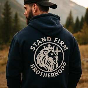 Könnte beinhalten: Marineblauer Kapuzenpullover mit weißer Grafik auf dem Rücken. Die Grafik zeigt einen Löwenkopf, eine Krone und ein Kreuz, umgeben von den Worten "STAND FIRM BROTHERHOOD". Die Person trägt eine schwarze Baseballkappe.
