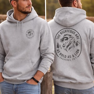 May include: Pale grey hoodie with a front pocket and drawstring hood. The front has a circular graphic with a lion and text. The back displays a larger graphic with a lion, trees, and the text "THE RIGHTEOUS ARE AS BOLD AS A LION PROVERBS 28:1."