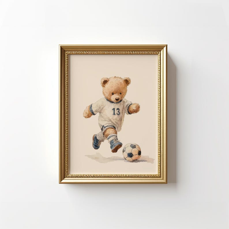 May include: A framed watercolor illustration of a light brown teddy bear wearing a white soccer jersey with the number 13 in blue, white shorts, and blue soccer cleats, actively kicking a black and white soccer ball on a light beige background.