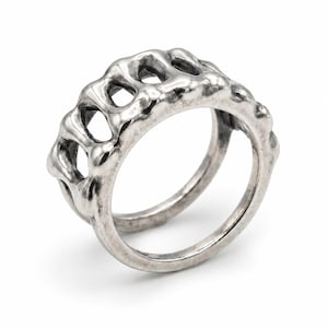 May include: A silver ring with an unusual, textured design. The ring has a series of connected, irregular shapes with open spaces, giving it a unique and modern look. The band is smooth and simple.