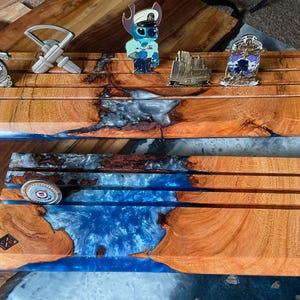 May include: Two rectangular wooden display stands featuring horizontal grooves for holding challenge coins. The stands are crafted from natural wood with vibrant blue epoxy resin accents. Several metal challenge coins are inserted into the slots.