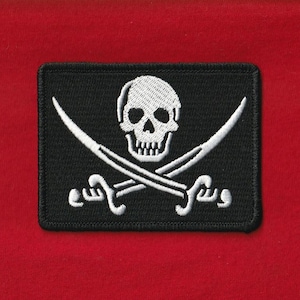 May include: Black rectangular patch featuring a white skull and crossbones design. Two curved white swords are crossed beneath the skull. The patch is on a red background, creating a striking contrast. The patch is likely an emblem or a decorative element.