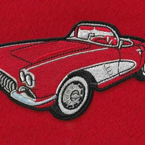 May include: An embroidered patch featuring a red vintage convertible sports car with white side panel detailing, black outlines, and silver-toned accents on the wheels, headlights, and grille, set against a solid red fabric background.