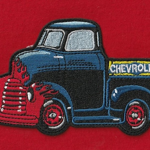 May include: An embroidered patch featuring a vintage pickup truck design. The truck has a blue cab, black body, and red front end with flame detailing. The word CHEVROLET is stitched in white on a yellow rectangular background on the truck bed.