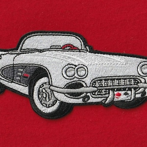 May include: An embroidered patch featuring a white vintage convertible sports car with black detailing, a red steering wheel, and a small license plate with red and black accents, set against a solid red fabric background.