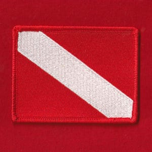 Può includere: Una toppa rettangolare rossa con una striscia diagonale bianca. La toppa ha un bordo rosso ed è probabilmente un emblema o un'insegna. Il design è semplice e audace, con un netto contrasto tra lo sfondo rosso e la striscia bianca.
