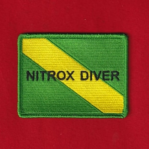 May include: Embroidered patch with a green background and a yellow diagonal stripe. The text "NITROX DIVER" is stitched in black. The patch has a green border and is rectangular in shape.