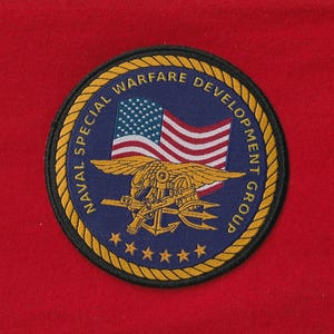 以下が含まれることがあります： 「NAVAL SPECIAL WARFARE DEVELOPMENT GROUP」の文字が金色で書かれた円形のパッチ。パッチには、アメリカ国旗、ワシ、錨、三叉の槍が描かれています。パッチは金色のロープのデザインで縁取られ、6つの金色の星があります。