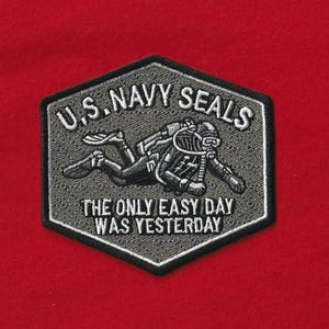 May include: A gray and black embroidered patch with the text "U.S. Navy Seals" and "The Only Easy Day Was Yesterday" on a red background. The patch features a diver in a diving suit.
