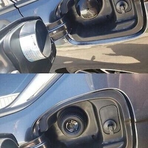 May include: Close-up of a car's fuel door and gas cap. The fuel door is open, revealing the gas cap and the fuel filler neck. The car's body is a dark color, and the fuel door has a chrome trim.