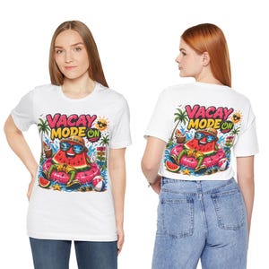 Pode incluir: Camiseta branca com um gráfico colorido de uma fatia de melancia usando óculos de sol e chapéu, flutuando em um anel inflável rosa. O texto "VACAY MODE ON" está acima da melancia.