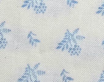 Könnte beinhalten: Nahaufnahme eines weißen Stoffes mit einem sich wiederholenden Muster aus hellblauen Blumen- und Blattmotiven. Das Design zeigt stilisierte Blumen und kleine Blattgruppen, die einen zarten, allover-Druck erzeugen. Der Stoff hat ein leicht strukturiertes Aussehen.
