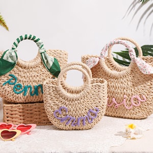 May include: Three woven straw handbags with rounded handles. The left bag features a green scarf and the name Penny in teal. The center bag displays the name Emma in purple. The right bag has a floral scarf and the name Asia in pink.